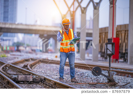 Engineer railway under checking construction process train testing and checking railway work on railroad station with radio communication .Engineer wearing safety uniform and safety helmet in work. Engineer railway under checking construction process train testing and checking railway work on railroad station with radio communication .Engineer wearing safety uniform and safety helmet in work. 87697879