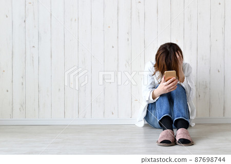 A woman scratching her head looking at her smartphone 87698744