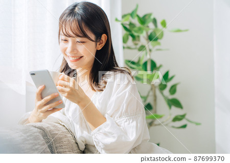 Woman sitting on a sofa and looking at a smartphone 87699370