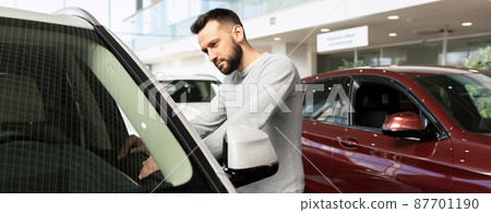 a man carefully examines new cars in a car dealership 87701190