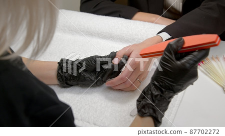 A close-up of a master doing a manicure to a young girl in a beauty salon. The concept of nails, manicure, beauty, fashion. A close-up of a master doing a manicure to a young girl in a beauty salon. The concept of nails, manicure, beauty, fashion. 87702272