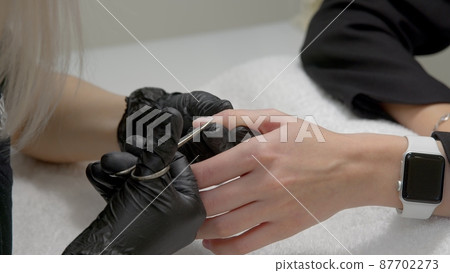 A close-up of a master doing a manicure to a young girl in a beauty salon. The concept of nails, manicure, beauty, fashion. A close-up of a master doing a manicure to a young girl in a beauty salon. The concept of nails, manicure, beauty, fashion. 87702273