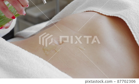 Pouring massage oil on attractive belly of young slim woman. Concept of body care and alternative medicine 87702306