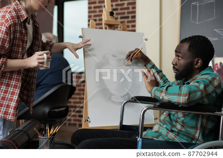 Painter teacher showing drawing technique to impaired student 87702944
