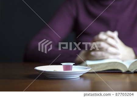 Holy Communion wine and bread with woman praying at the background. 87703204