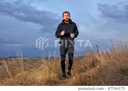 Athlete Strong Male Running Through the field. Man Wearing Black sportive wear 87704173