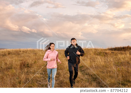 Young Couple Running On Field In Morning. Caucasian Man And Woman On Jogging Workout 87704212