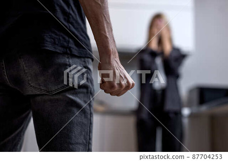 Aggressive Angry Husband Going To Beat Unhappy Crying Wife Standing In Background. Aggressive Angry Husband Going To Beat Unhappy Crying Wife Standing In Background. 87704253