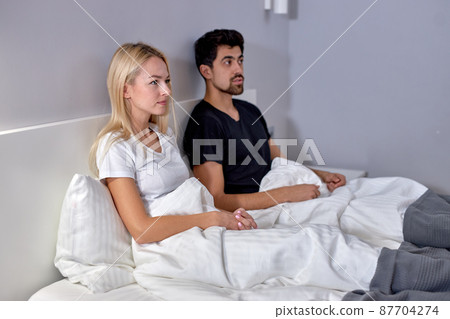 Couple watching tv in bed in cozy room at home looking at side, family concept Couple watching tv in bed in cozy room at home looking at side, family concept 87704274