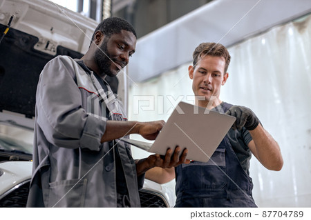 team of diverse mechanics in uniform examining car while working in auto service team of diverse mechanics in uniform examining car while working in auto service 87704789