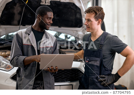 Computer Car Tuning. two Smiling auto mechanic testing a car engine connected to laptop. 87704795