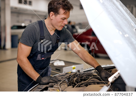 Car mechanic looking inside of engine in garage. Car motor repair. Problems and solutions 87704837