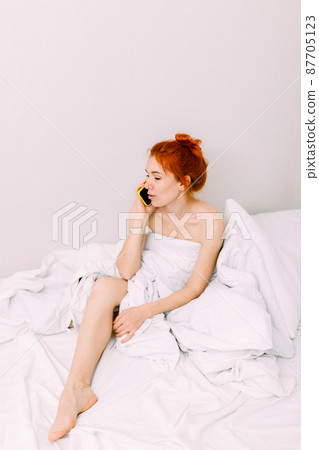 Portrait of a young beautiful redhead woman talking on the phone in bed Portrait of a young beautiful redhead woman talking on the phone in bed 87705123