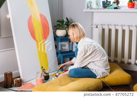 Young woman artist is painting at home in a creative studio setting. Young woman artist is painting at home in a creative studio setting. 87705272