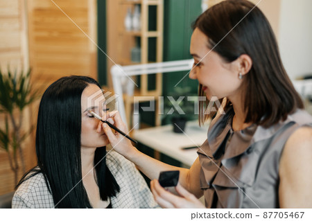 A professional makeup artist working with a beautiful young woman applies eye shadow A professional makeup artist working with a beautiful young woman applies eye shadow 87705467