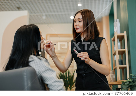 A make-up artist makes makeup for a girl in the salon, applies lipstick, completes the image. The concept of beauty and self-care A make-up artist makes makeup for a girl in the salon, applies lipstick, completes the image. The concept of beauty and self-care 87705469