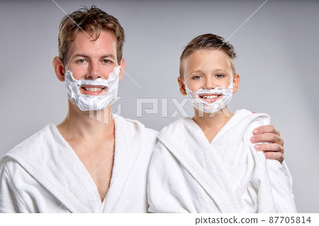 young father and teenage son with shaving foam on faces are looking at camera smiling 87705814