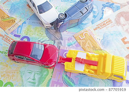 New Zealand dollar bills and tow trucks and white cars colliding with towed red cars and blue cars rolling over 87705919