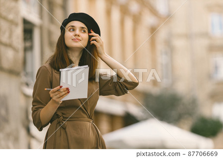Girl in dress and black hat painting a sketch while standing on a street 87706669