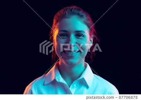Half-length portrait of young pretty girl in white shirt isolated on dark background in blue neon light, filter. Concept of emotions, fashion, youth Half-length portrait of young pretty girl in white shirt isolated on dark background in blue neon light, filter. Concept of emotions, fashion, youth 87706878