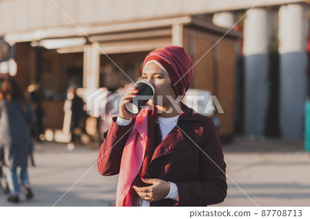 Young Arabic muslim woman in hijab walking at street seafront and drinking coffee take away 87708713