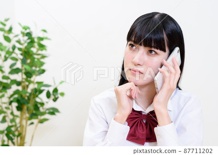 A high school girl who holds a smartphone and puts her hand on her chin to make a call Girls Talk Make a call Question consultation 87711202