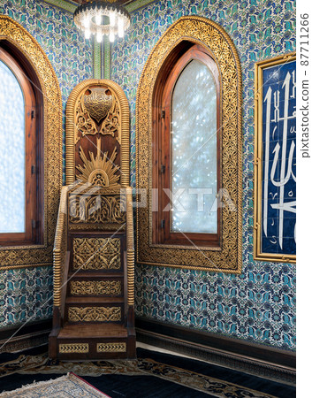 Wooden golden ornate minbar (Platform), wooden arched window framed by golden ornate floral pattern, and ceramic tiles wall with floral blue patterns Wooden golden ornate minbar (Platform), wooden arched window framed by golden ornate floral pattern, and ceramic tiles wall with floral blue patterns 87711266