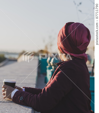 Young Arabic muslim woman in hijab standing at street seafront and drinking coffee take away - copy space and place for advertising Young Arabic muslim woman in hijab standing at street seafront and drinking coffee take away - copy space and place for advertising 87711790