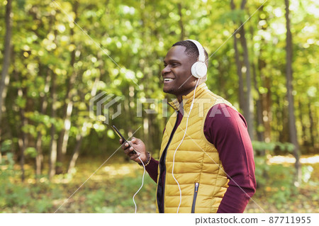 African american man listens music in spring park copy space and place for advertising. Gadget, app and streaming service concept 87711955