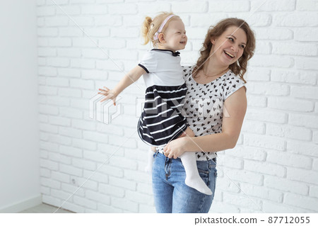 Mother holds her child with hearing aids and cochlear implants on white brick wall with copy space and place for advertising . Deaf and health concept 87712055