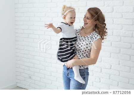 Mother holds her child with hearing aids and cochlear implants on white brick wall with copy space and place for advertising . Deaf and health concept 87712056
