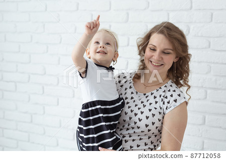 Mother holds her child with hearing aids and cochlear implants on white brick wall with copy space and place for advertising . Deaf and health concept 87712058
