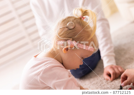 Baby with cochlear implants having fun at home. Deafness and medical technology concept. 87712125