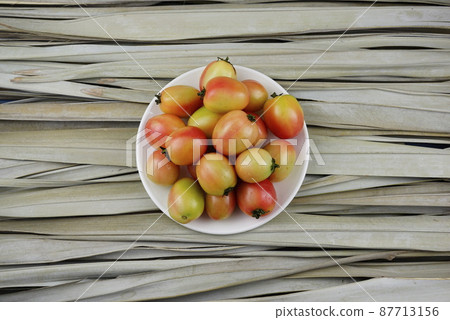Top view of fresh pink, marigold egg tomatoes in white plate, dish. Food, still life photography, with dried palm leaves background. Organic, minimal image style. 87713156