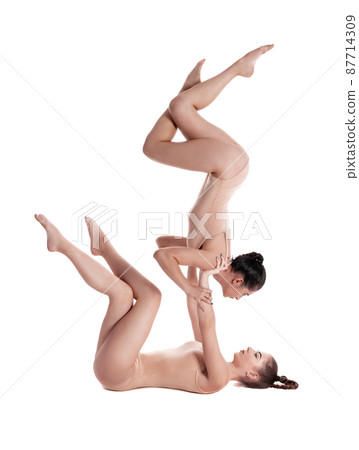 Two flexible girls gymnasts in beige leotards are performing exercises upside down using support and posing isolated on white background. Close-up. 87714309