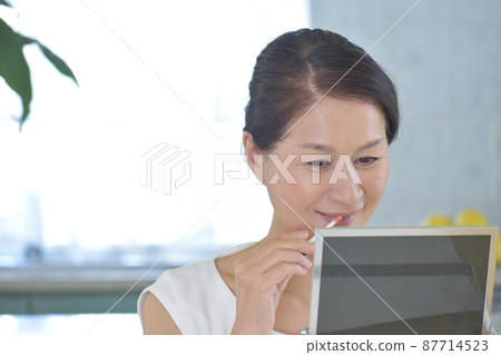 一個女人一邊照鏡子一邊塗口紅 87714523