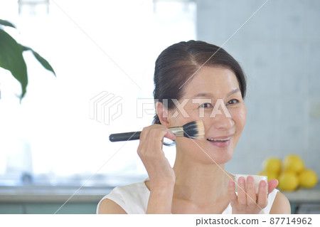 60 多歲的女人,一邊在臉頰上撒粉一邊微笑 60 多歲的女人,一邊在臉頰上撒粉一邊微笑 87714962