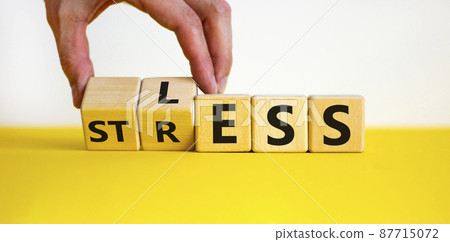 Having less stress or being stress-less. The word 'STRESS' and 'LESS' on wooden cubes. Male hand. Beautiful yellow table, white background, copy space. Business and psychological less stress concept. 87715072