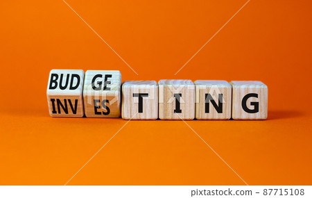 Budgeting or investing symbol. Turned wooden cubes and changed the word investing to budgeting. Beautiful orange table, orange background, copy space. Business and budgeting or investing concept. 87715108