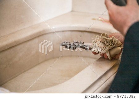 An Armenian priest with a cross and a bible performs the rite of baptism over the font. 87715382
