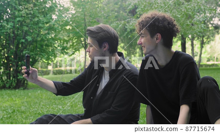 Two young guys are photographed on the phone in nature in the summer. LGBT Two young guys are photographed on the phone in nature in the summer. LGBT 87715674