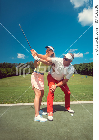 Golf pro teaching a woman student of the driving range 87716236