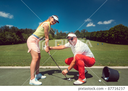 Golf pro teaching a woman student of the driving range 87716237