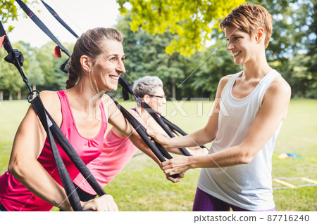 Smiling young woman exercises using suspension training 87716240