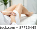 Skinny woman with beautiful legs with well-groomed leather and crossed arms lies on a white beauty table 87716445