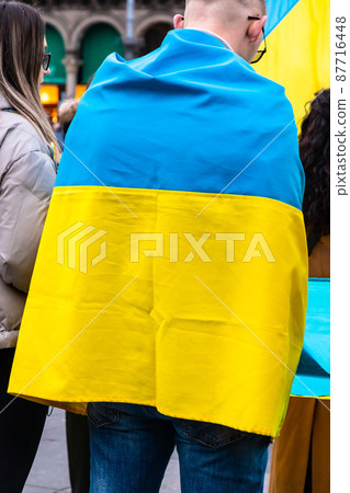 Young man wrapped in the Ukrainian flag in a protest against Russia invasion Young man wrapped in the Ukrainian flag in a protest against Russia invasion 87716448