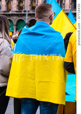Young man wrapped in the Ukrainian flag in a protest against Russia invasion Young man wrapped in the Ukrainian flag in a protest against Russia invasion 87716450