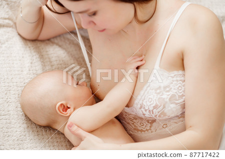 a mother feeds the baby with breast milk on the bed. the breastfeeding.  87717422