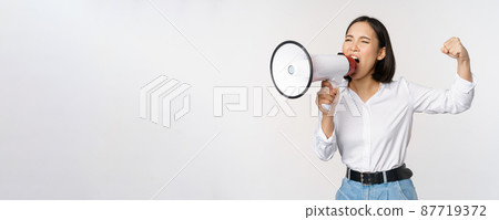 Enthusiastic asian woman, girl activist shouting at protest, using megaphone, looking confident, talking in loudspeaker, protesting, standing over white background Enthusiastic asian woman, girl activist shouting at protest, using megaphone, looking confident, talking in loudspeaker, protesting, standing over white background 87719372