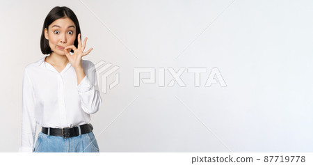 Mouth shut. Young asian woman seal lips, showing taboo dont speak, keep quiet sign, hiding secret, standing over white background Mouth shut. Young asian woman seal lips, showing taboo dont speak, keep quiet sign, hiding secret, standing over white background 87719778